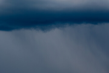 Thick storm clouds stretch across the sky with a visible curtain of rain falling below, creating a...