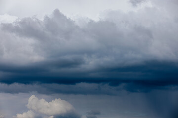 Obraz premium Dark, dense storm clouds gather across the sky, with heavy rain visible in the distance and a few lighter clouds at the bottom ample copy space.