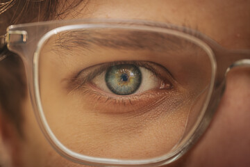 Close-up of a human eye framed by clear glasses, showcasing intricate iris detail and subtle...
