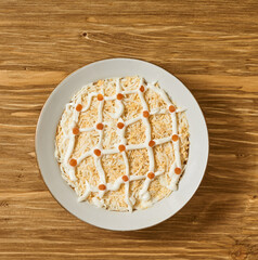 Layered salad with mayonnaise net and red caviar dots served in a white bowl on wooden surface. Concept of traditional Russian cuisine