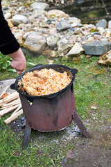 Top view of a Tajik woman cooking hot pilaf in a cauldron over an open fire, stirring the...