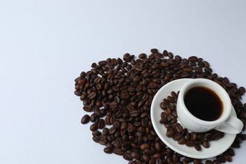 Hot coffee in a white coffee cup and many coffee beans scattered around 