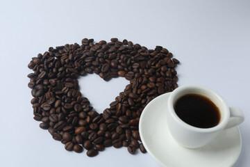 Hot coffee in a white coffee cup and many coffee beans scattered around 