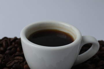 Hot coffee in a white coffee cup and many coffee beans scattered around 