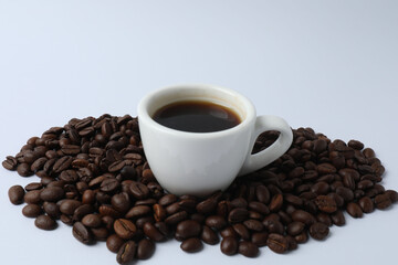 Hot coffee in a white coffee cup and many coffee beans scattered around 