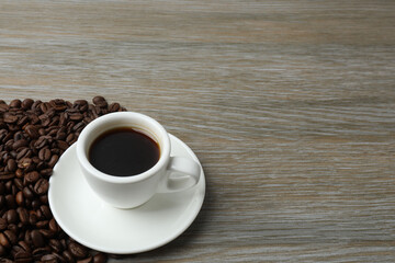 Hot coffee in a white coffee cup and many coffee beans scattered around 