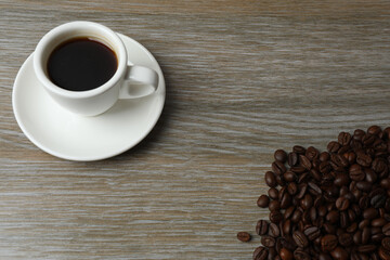 Hot coffee in a white coffee cup and many coffee beans scattered around 