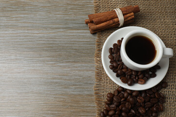 Hot coffee in a white coffee cup and many coffee beans scattered around 