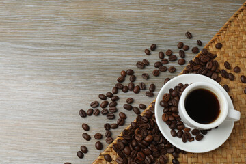 Hot coffee in a white coffee cup and many coffee beans scattered around 