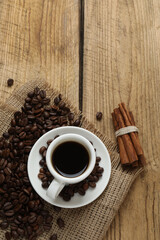 Hot coffee in a white coffee cup and many coffee beans scattered around 