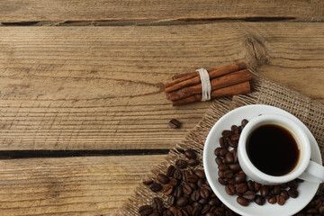 Hot coffee in a white coffee cup and many coffee beans scattered around 