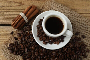 Hot coffee in a white coffee cup and many coffee beans scattered around 