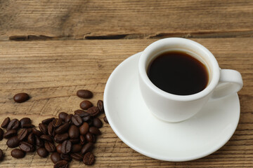 Hot coffee in a white coffee cup and many coffee beans scattered around 