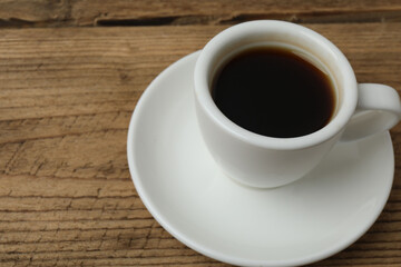 Hot coffee in a white coffee cup and many coffee beans scattered around 