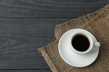 Hot coffee in a white coffee cup and many coffee beans scattered around 