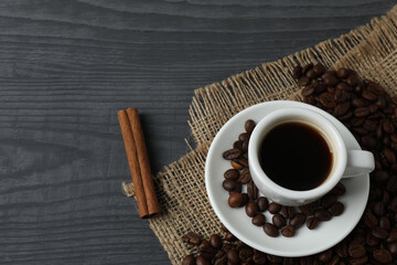 Hot coffee in a white coffee cup and many coffee beans scattered around 