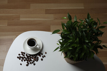 Hot coffee in a white coffee cup and many coffee beans scattered around 