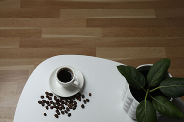 Hot coffee in a white coffee cup and many coffee beans scattered around 