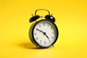 One black alarm clock on yellow background
