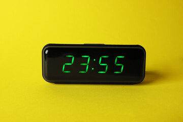 Digital alarm clock showing 23:55 o'clock on yellow background