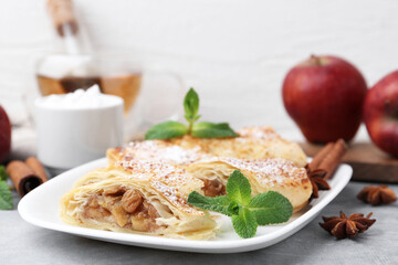 Tasty apple strudels with powdered sugar, mint and spices on light grey table, closeup