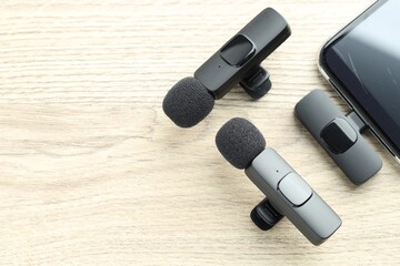 Lavalier microphones and smartphone with wireless receiver on wooden table, flat lay. Space for text