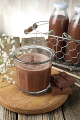 Tasty chocolate milk with shavings, pieces and flowers on wooden table
