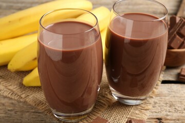 Tasty chocolate milk in glasses, pieces and bananas on wooden table, closeup