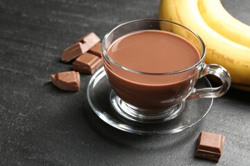 Tasty chocolate milk in glass cup, pieces and bananas on black table, closeup