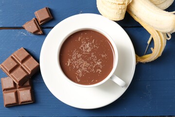 Tasty chocolate milk in cup, pieces and banana on blue wooden table, flat lay
