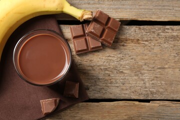 Tasty chocolate milk, pieces and banana on wooden table, flat lay. Space for text