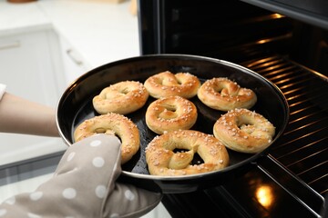 Woman taking baking dish with fresh pretzels out of oven, closeup