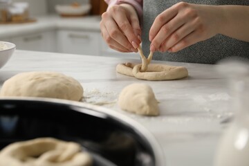 Woman shaping pretzels at table in kitchen, selective focus
