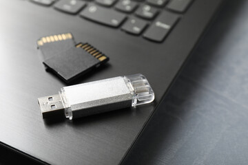 Usb flash drive, SD memory cards and laptop on grey textured table, closeup