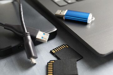 Flash drive, SD memory cards, external hard disk and laptop on gray table, closeup