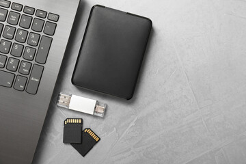 Flash drive, SD memory cards, external hard disk and laptop on gray textured table, flat lay. Space...