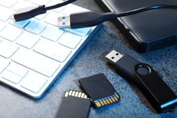 SD memory cards, USB flash drive, hard disk drive with cable and keyboard on dark grey table,...