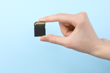 Woman holding SD memory card on light blue background, closeup
