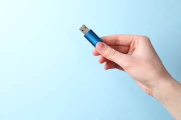 Woman holding USB flash drive on light blue background, closeup. Space for text