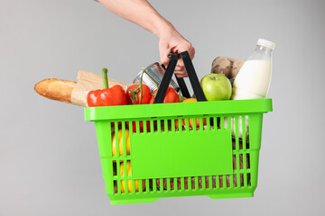 Man holding shopping basket with different products on grey background, closeup