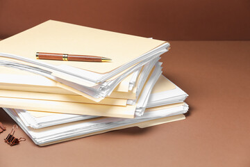 File folders with papers, pen and binder clip on brown background, closeup