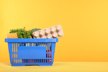 Shopping basket with different food products on yellow background, space for text