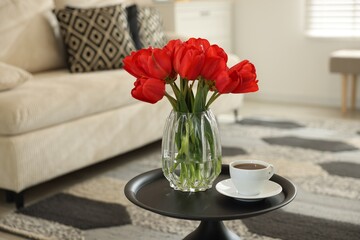 Beautiful red tulips in vase and tea on table indoors, space for text