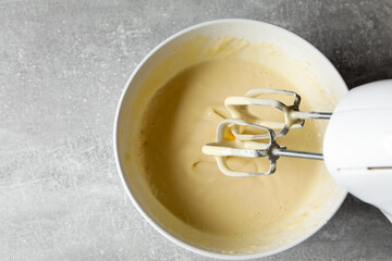 Hand mixer with whisks and bowl of dough on grey textured table, top view. Space for text