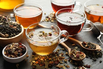 Different herbal teas and dry leaves on black table, closeup