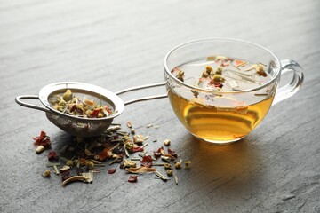 Delicious herbal tea and dry leaves on black table, closeup