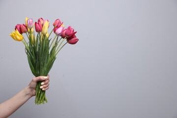 Woman with bouquet of beautiful tulips on light grey background, closeup. Space for text