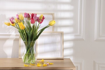 Bouquet of beautiful tulips and frames on wooden table indoors. Space for text