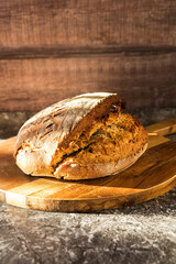 sourdough bread on a wooden cutting board at a stone table in sunlight with wooden background