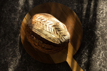 sourdough bread on a wooden cutting board at a stone table in sunlight